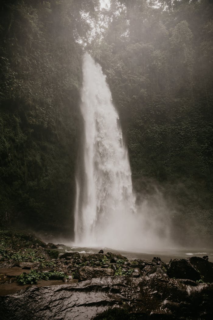 A stunning waterfall surrounded by lush greenery and mist in Bali, Indonesia.